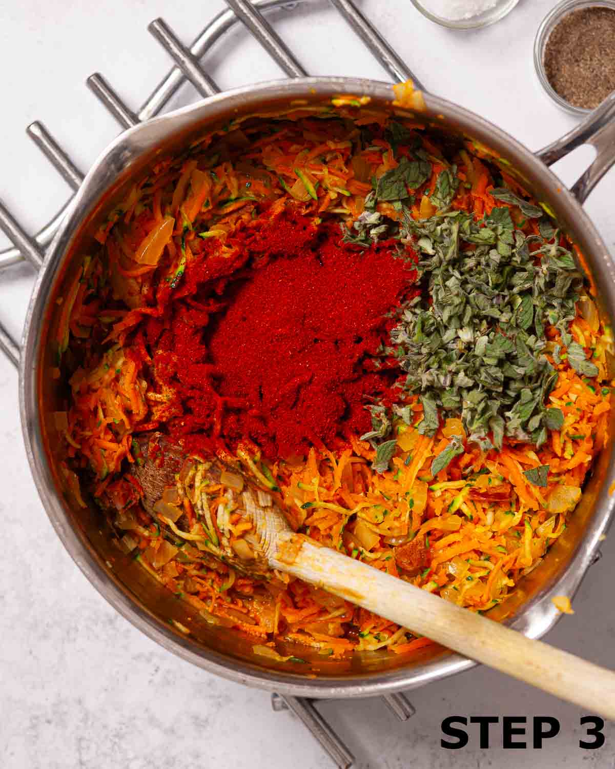 Paprika and oregano sprinkled into a pan containing ingredients for tomato, carrot and courgette soup.