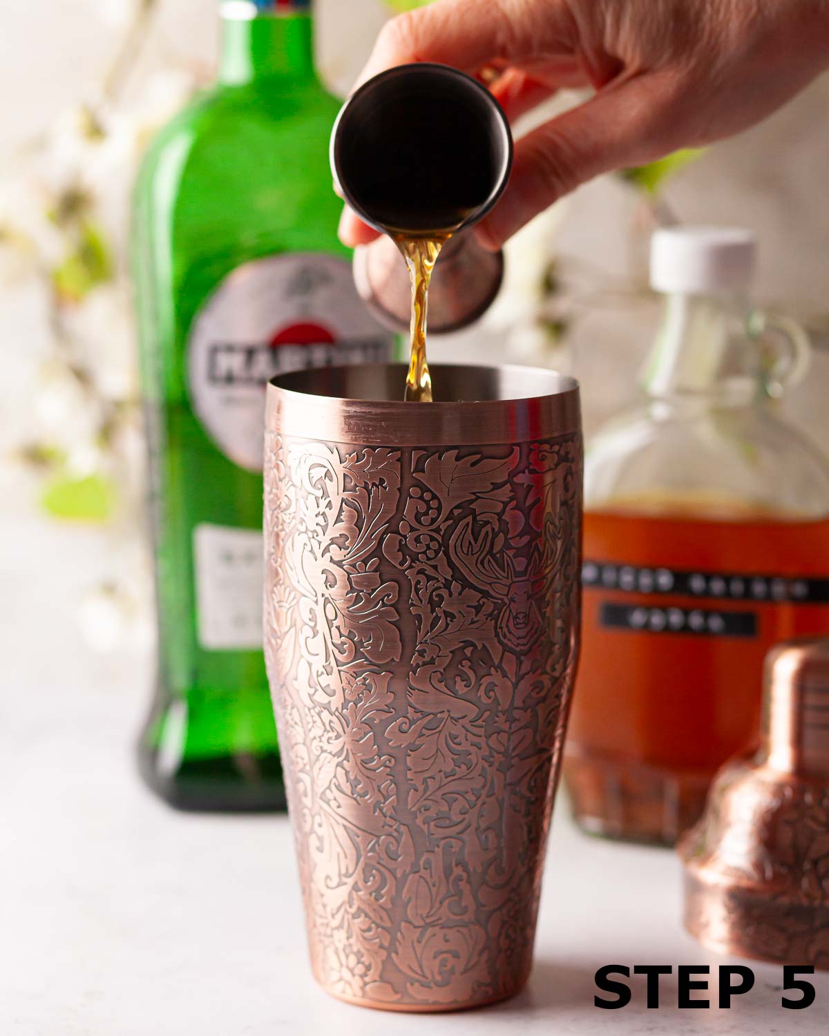 A person pouring hot cross bun vodka into a cocktail shaker.