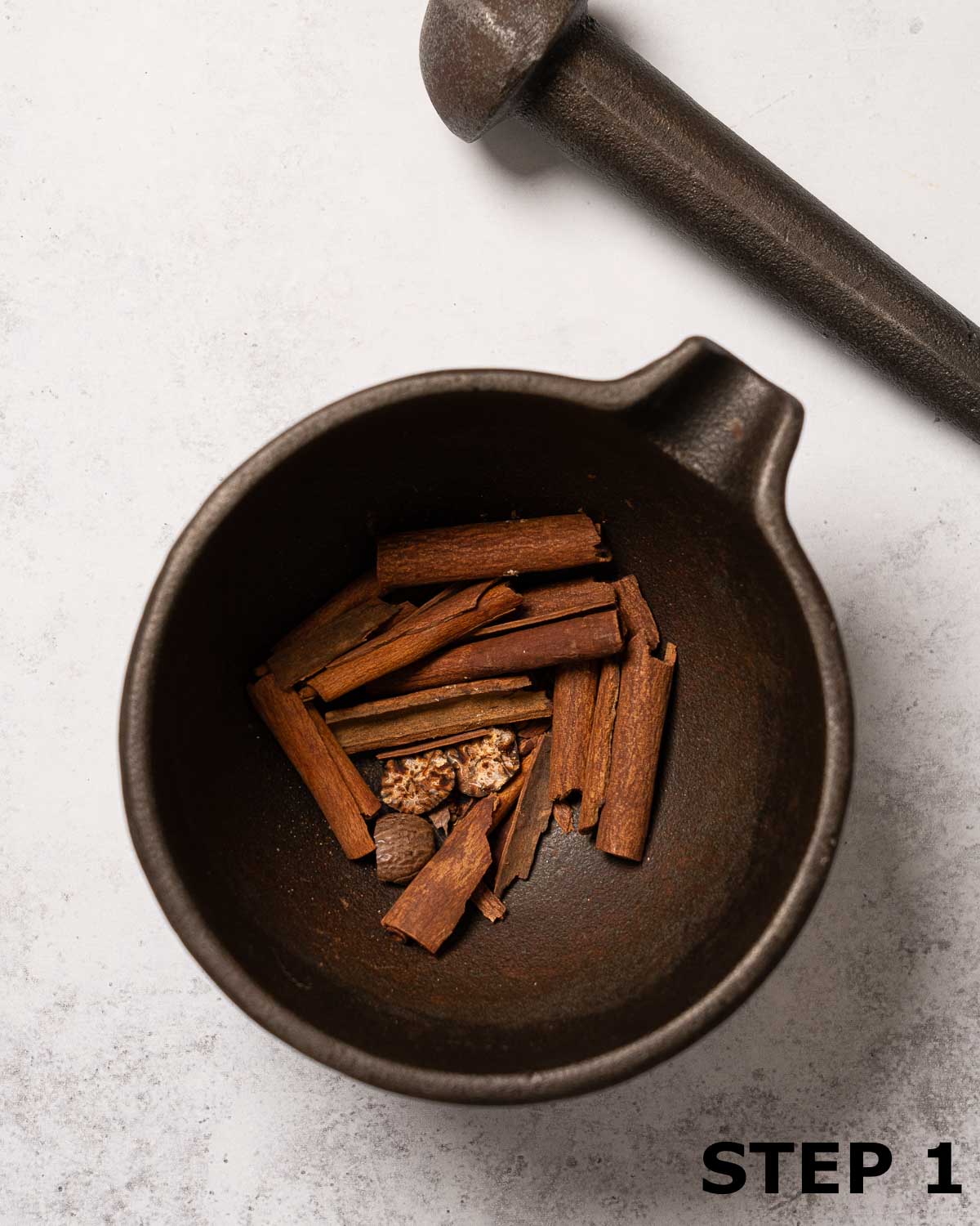 Broken cinnamon sticks and nutmeg in a mortar.