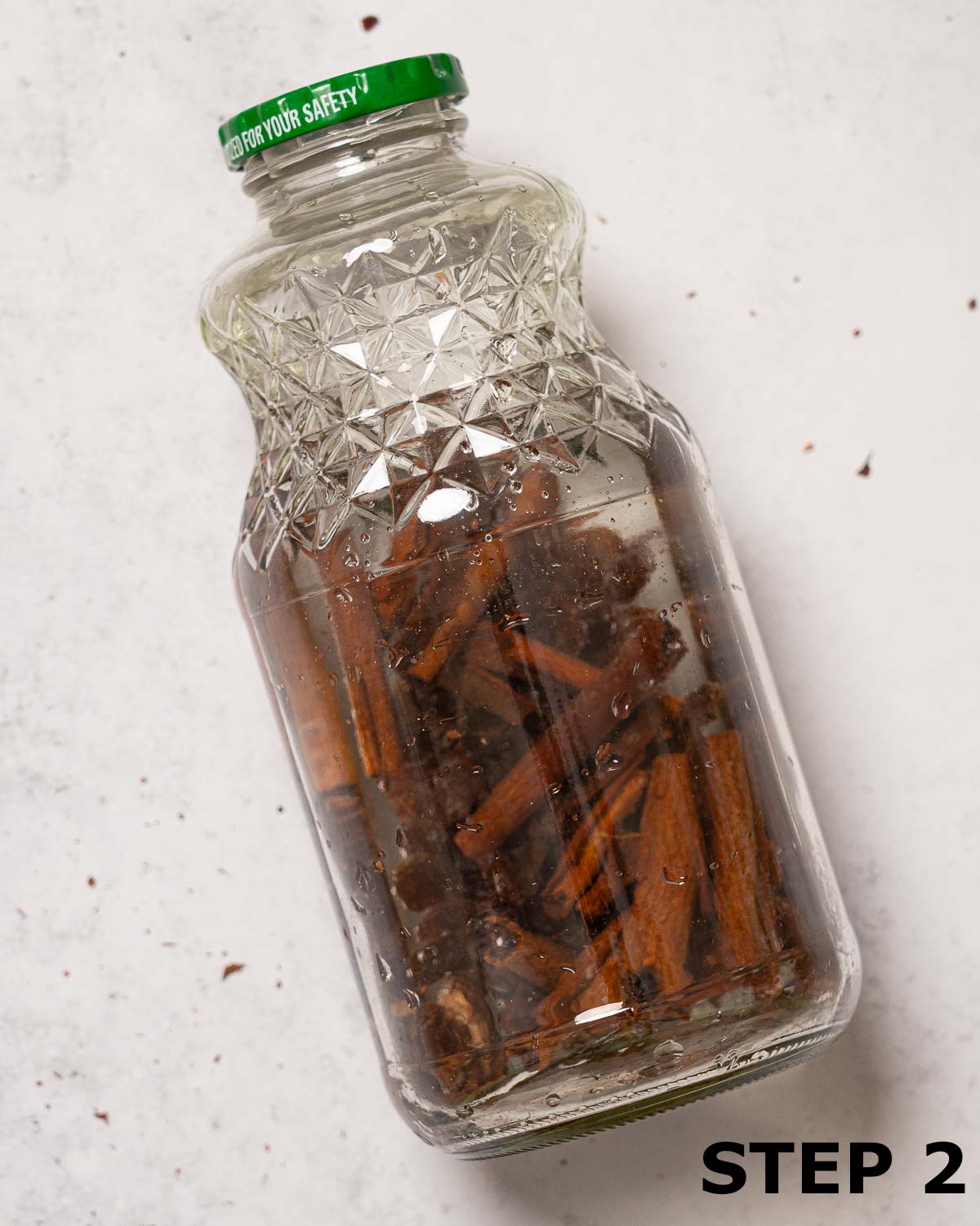 A glass jar cotaining vodka, cinnamon, nutmeg and raisins.