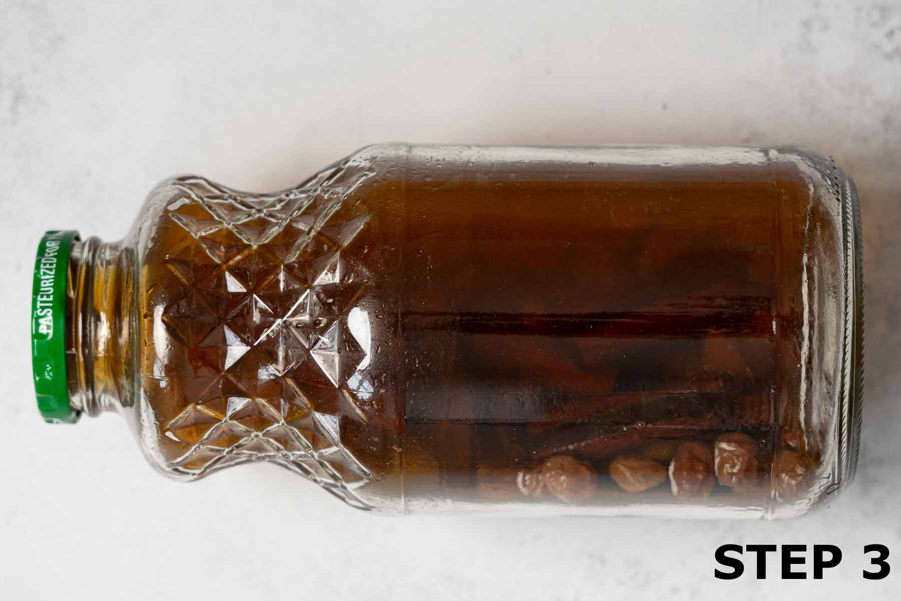 A glass jar containing vodka infused with dried fruit, cinnamon and nutmeg.