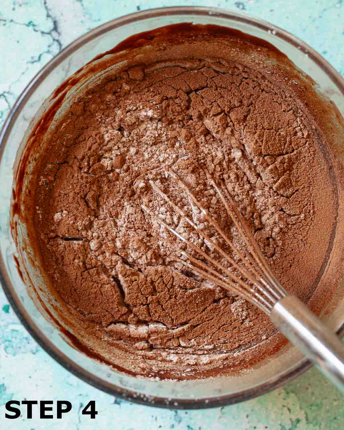 Sieved cocoa powder and flour in a bowl of brownie batter with a balloon whisk.