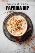 Labelled bowl of soured cream paprika dip topped with chives and paprika.