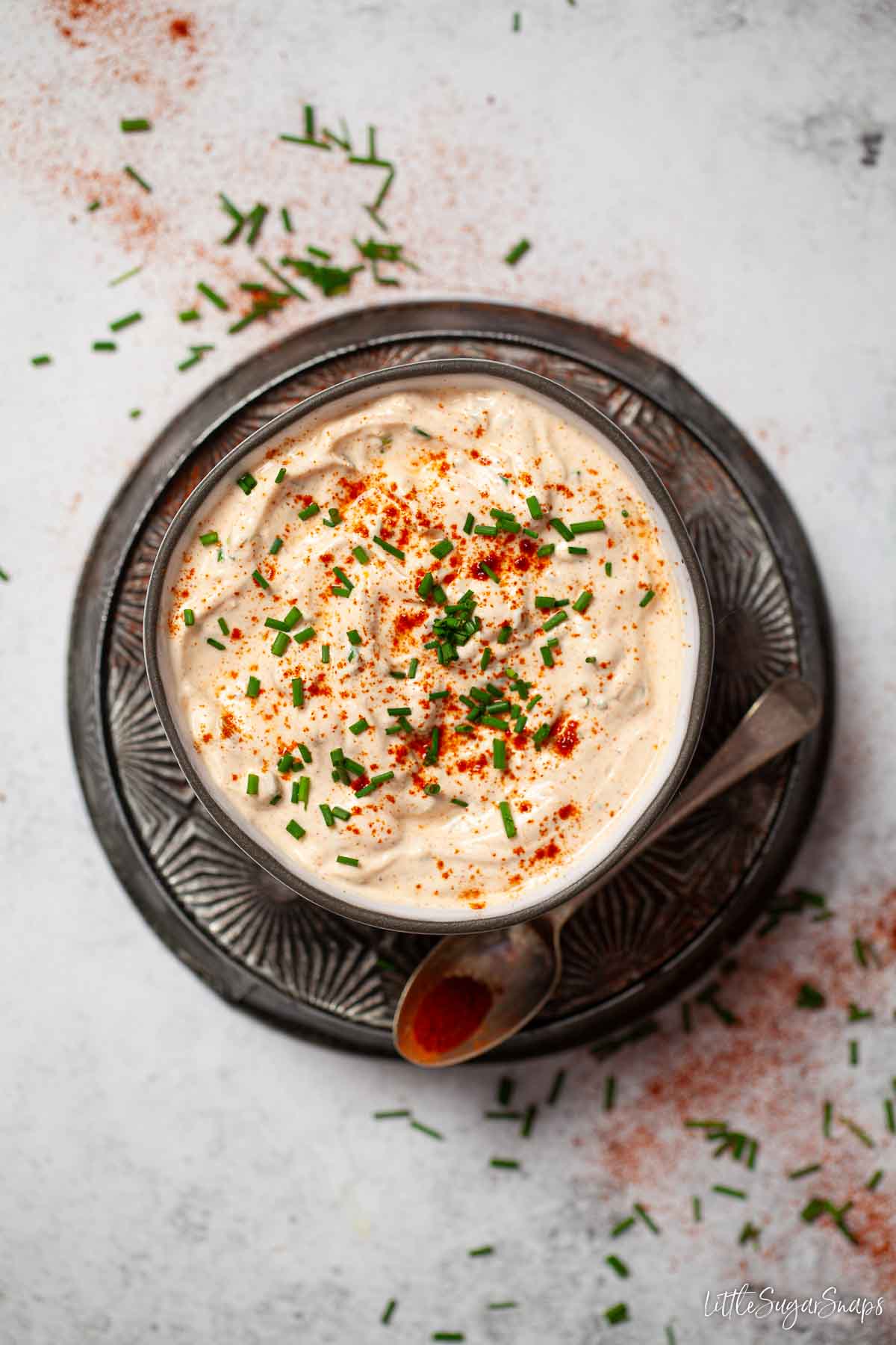 A bowl of soured cream paprika dip topped with chives and paprika.