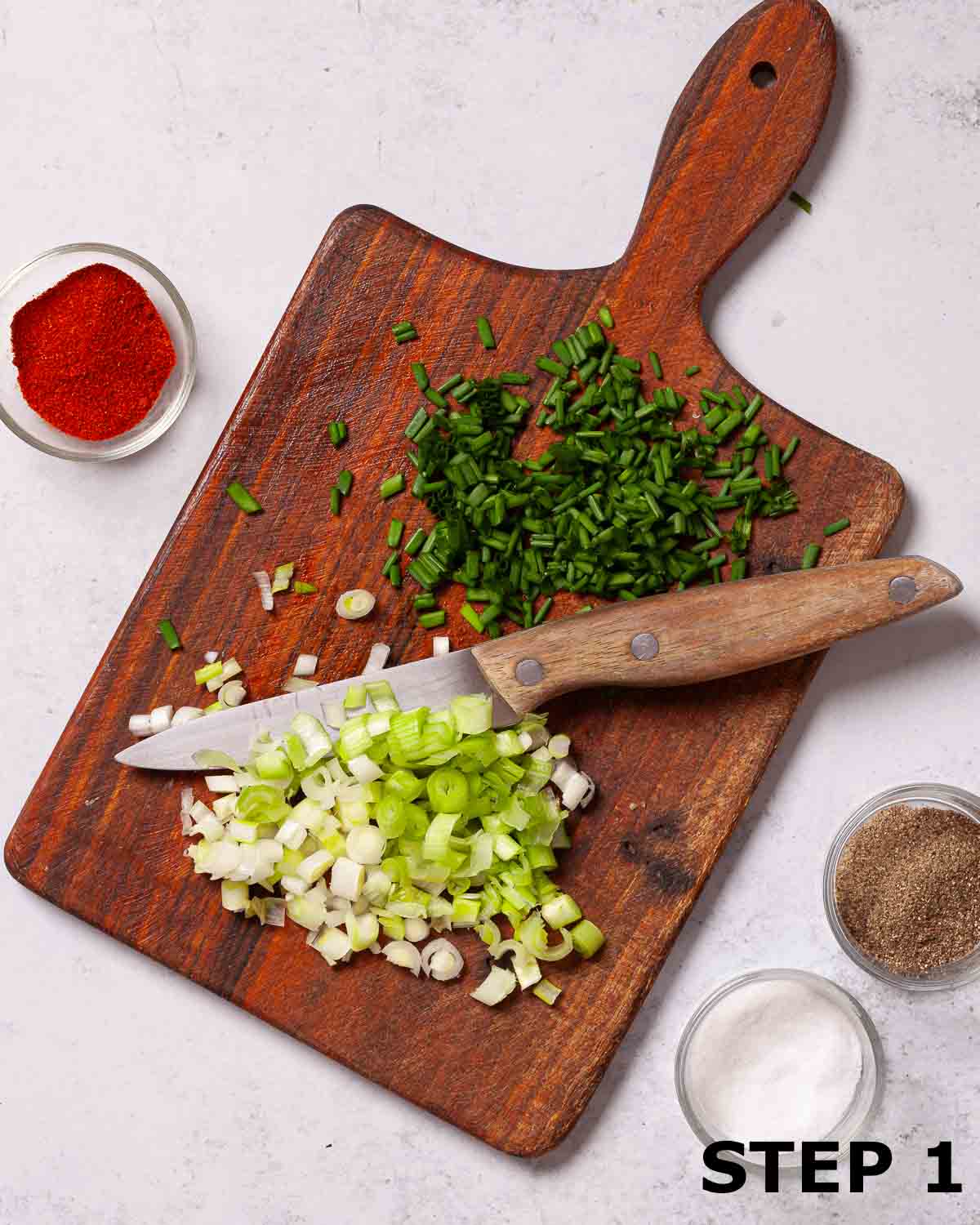 Chopped chives and chopped spring onions on a wooden board.
