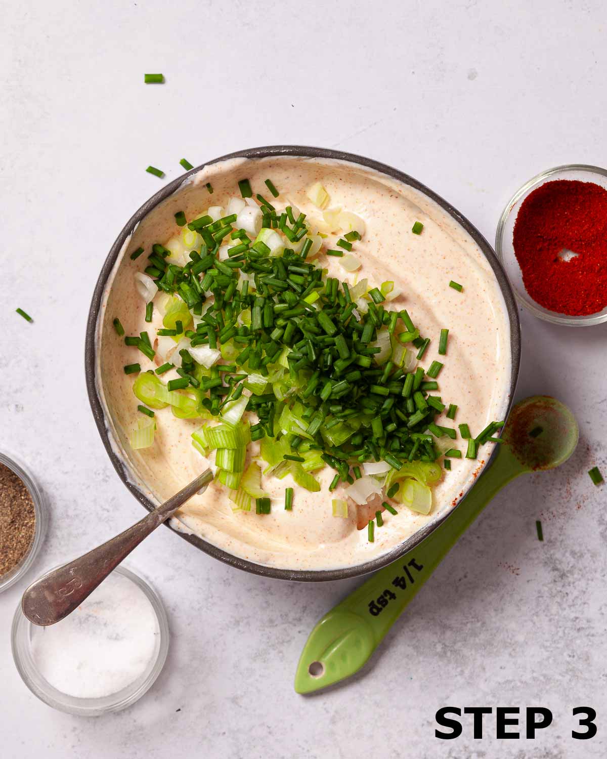 Chives and spring onions scattered over paprika dip in a mixing bowl.