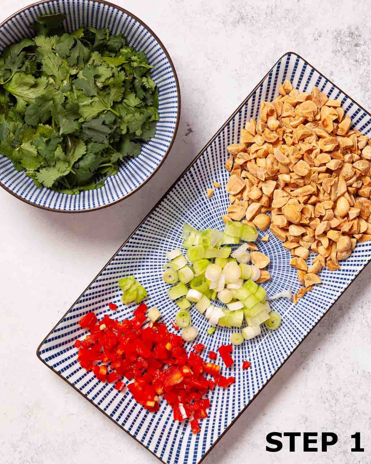 Chopped peanuts, red chilli and onion on an oblong plate with a bowl of coriander leaves.