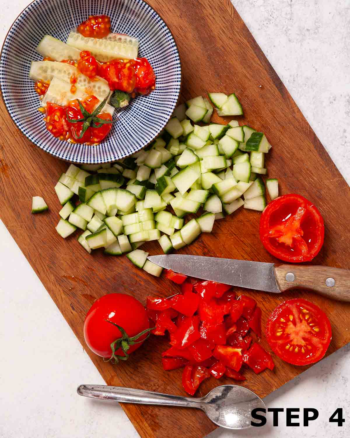 Diced cucumber and partially chopped tomatoes on a chopping board.