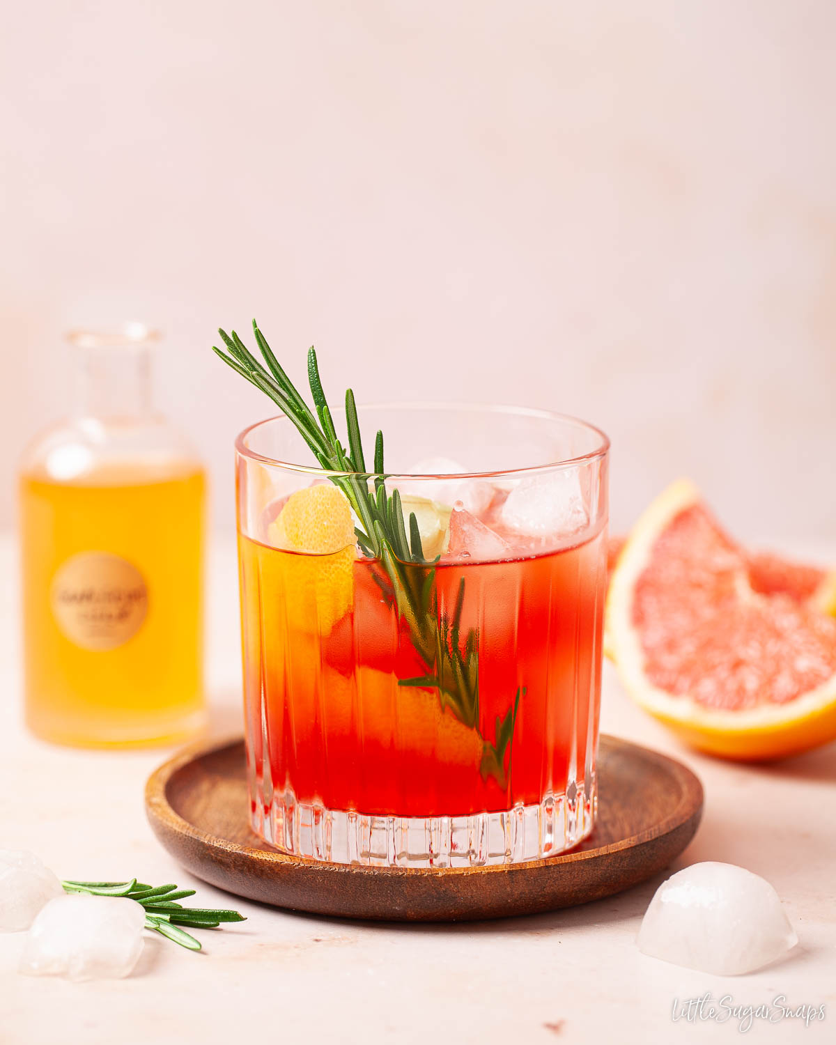 A grapefruit and gin cocktail with a bottle of grapefruit syrup in the background.