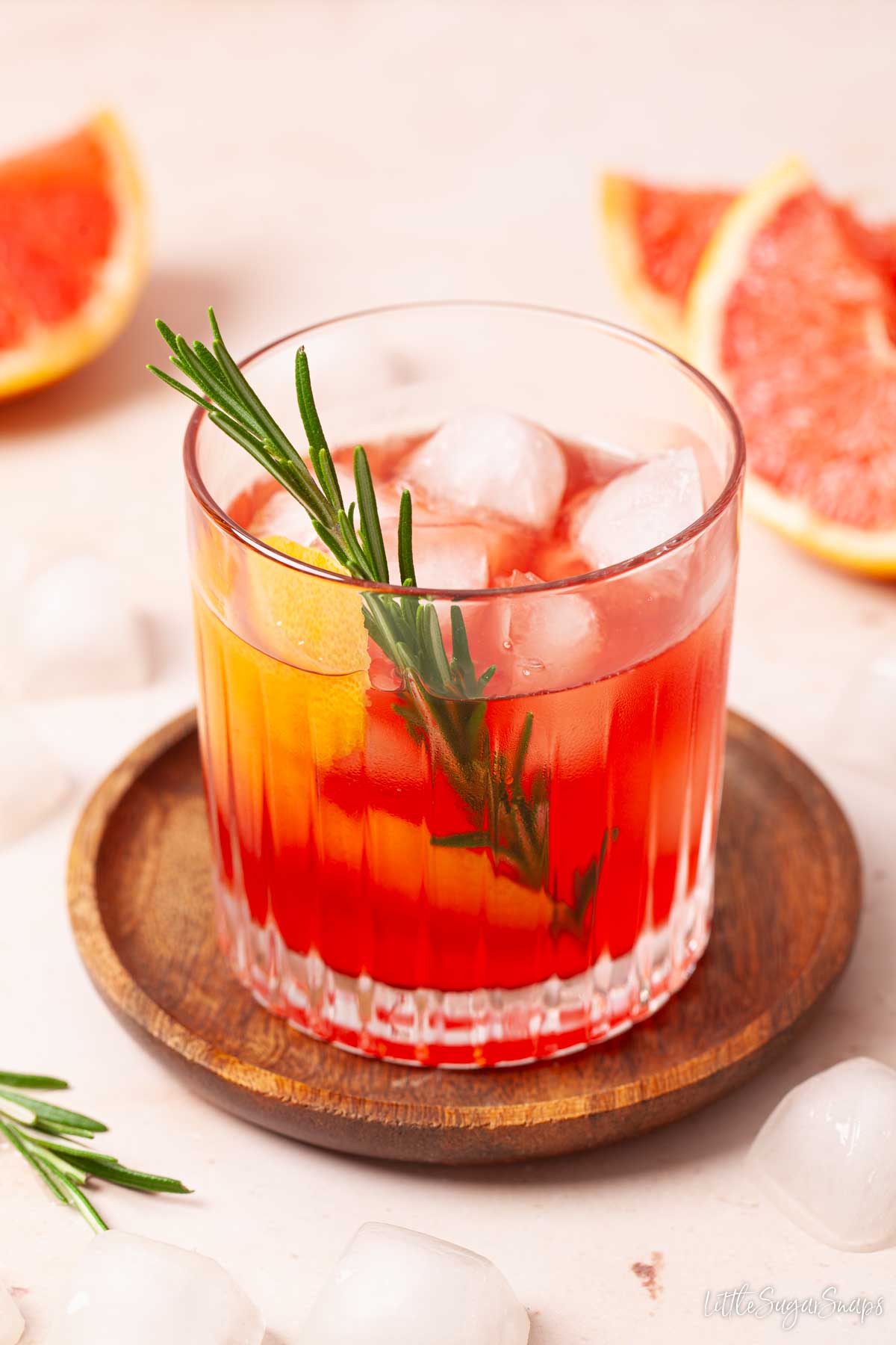 A grapefruit negroni cocktail garnished with grapefruit twist and fresh rosemary.