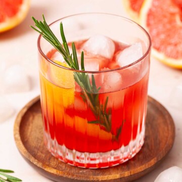 A grapefruit and gin cocktail garnished with grapefruit twist and fresh rosemary.