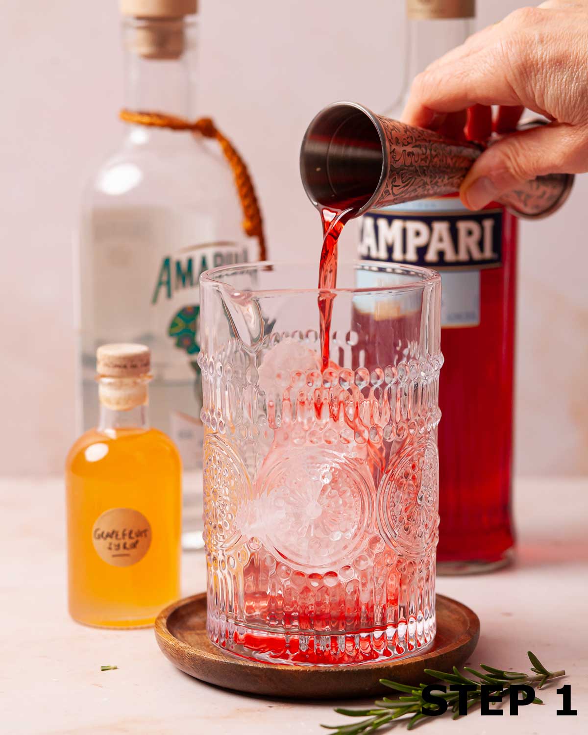 A person pouring Campari into a cocktail jug.