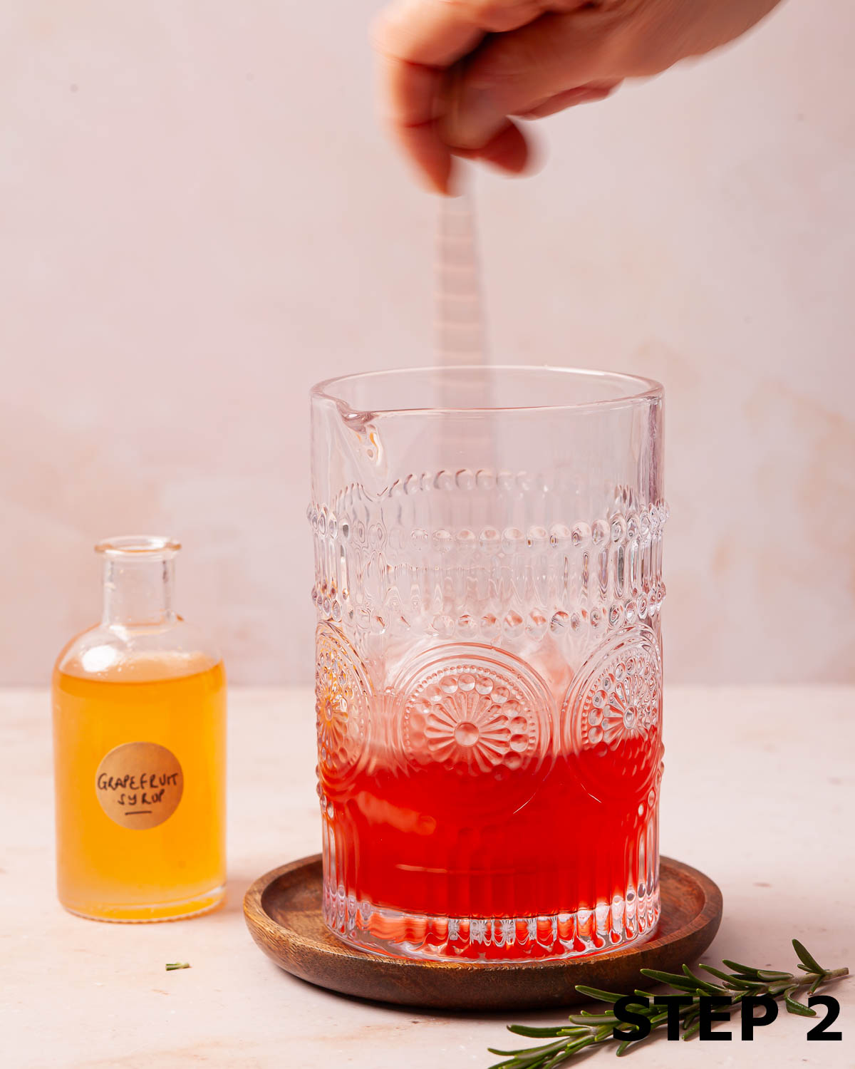 A person stirring a grapefruit syrup cocktail in a glass jug.