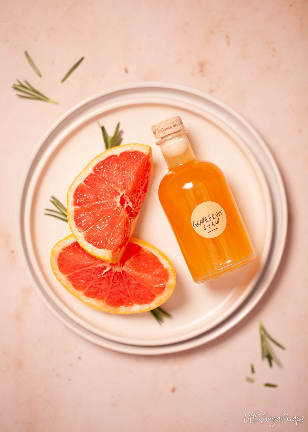 A bottle of grapefruit syrup on a plate with slices of red grapefruit.