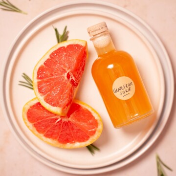 A bottle of grapefruit syrup on a plate with slices of red grapefruit.