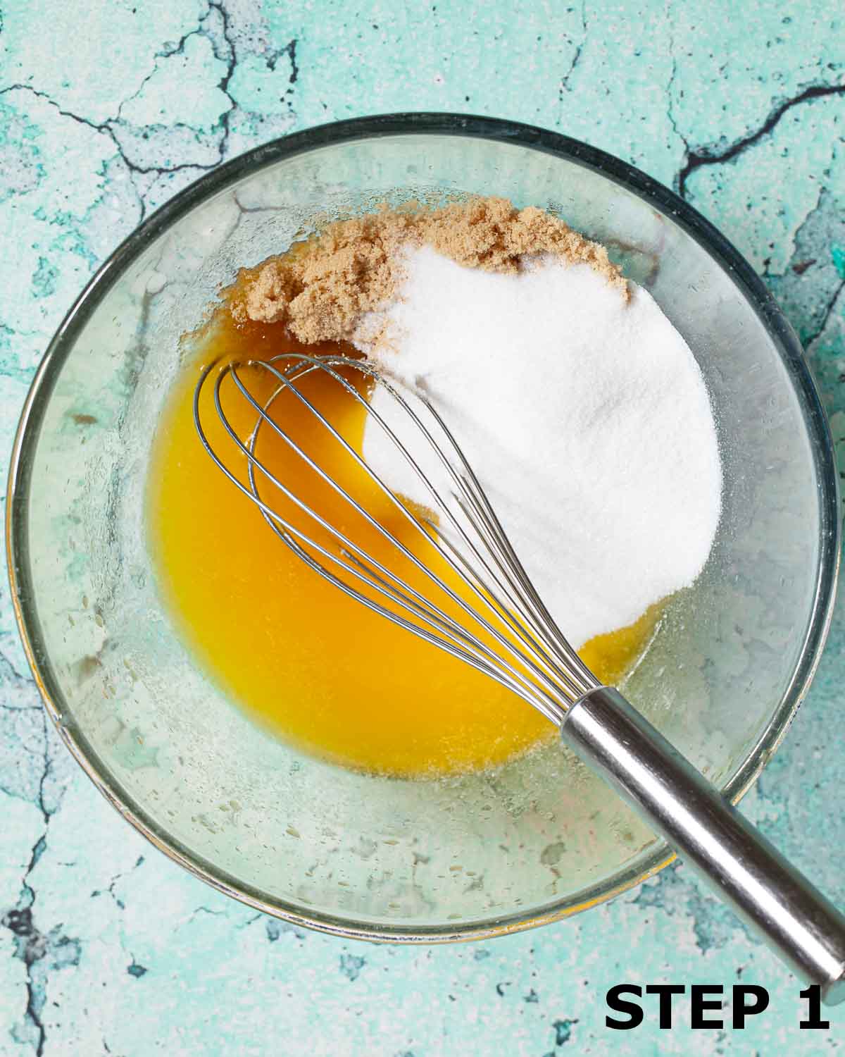 Melted butter, white sugar and brown sugar in a mixing bowl with a balloon whisk.