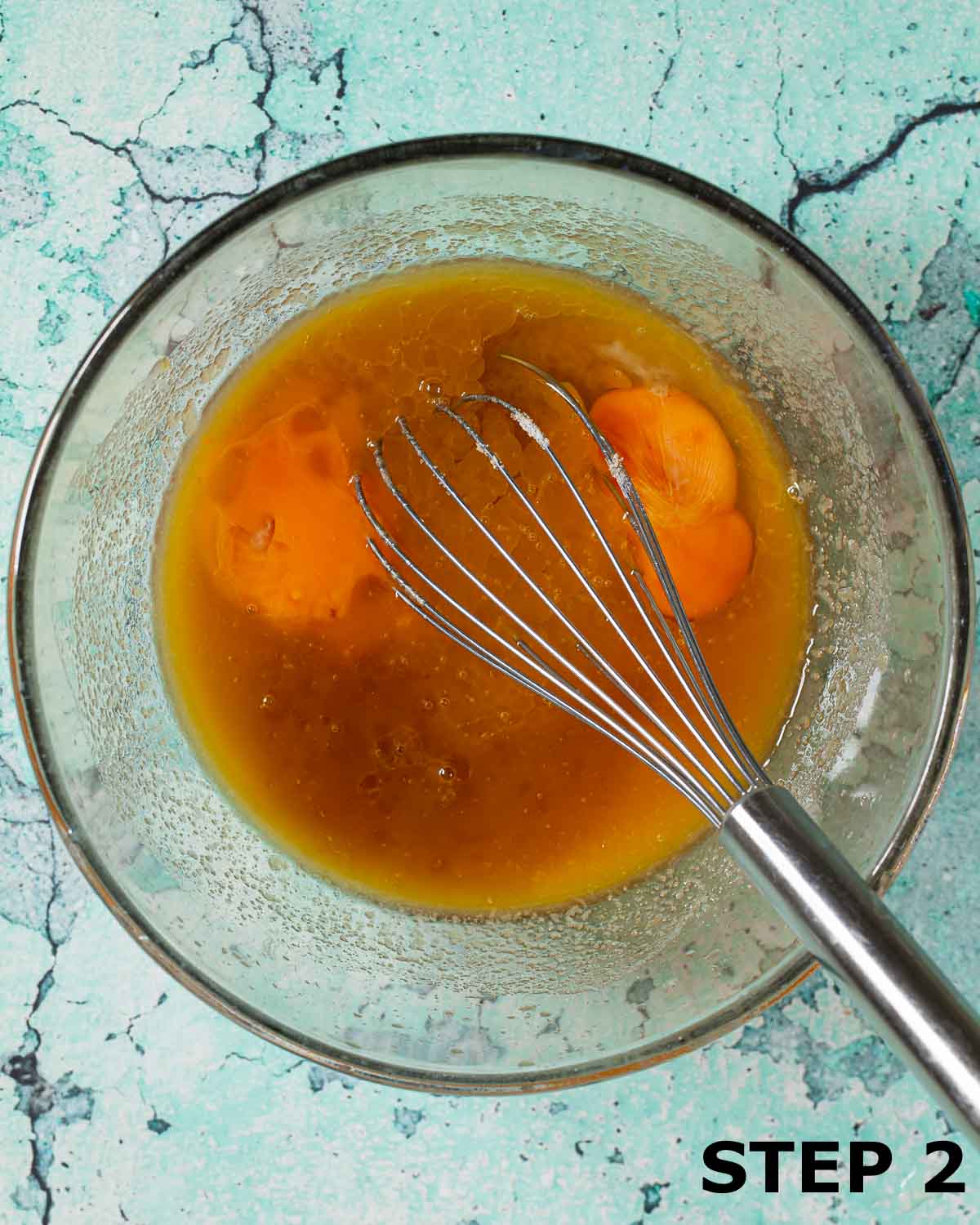 Eggs in a mixing bowl containing a blend of melted butter and sugar with a balloon whisk in it.