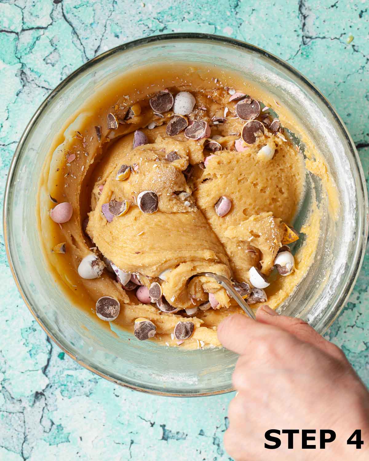 A person folding chopped Mini Egg pieces into cookie dough.