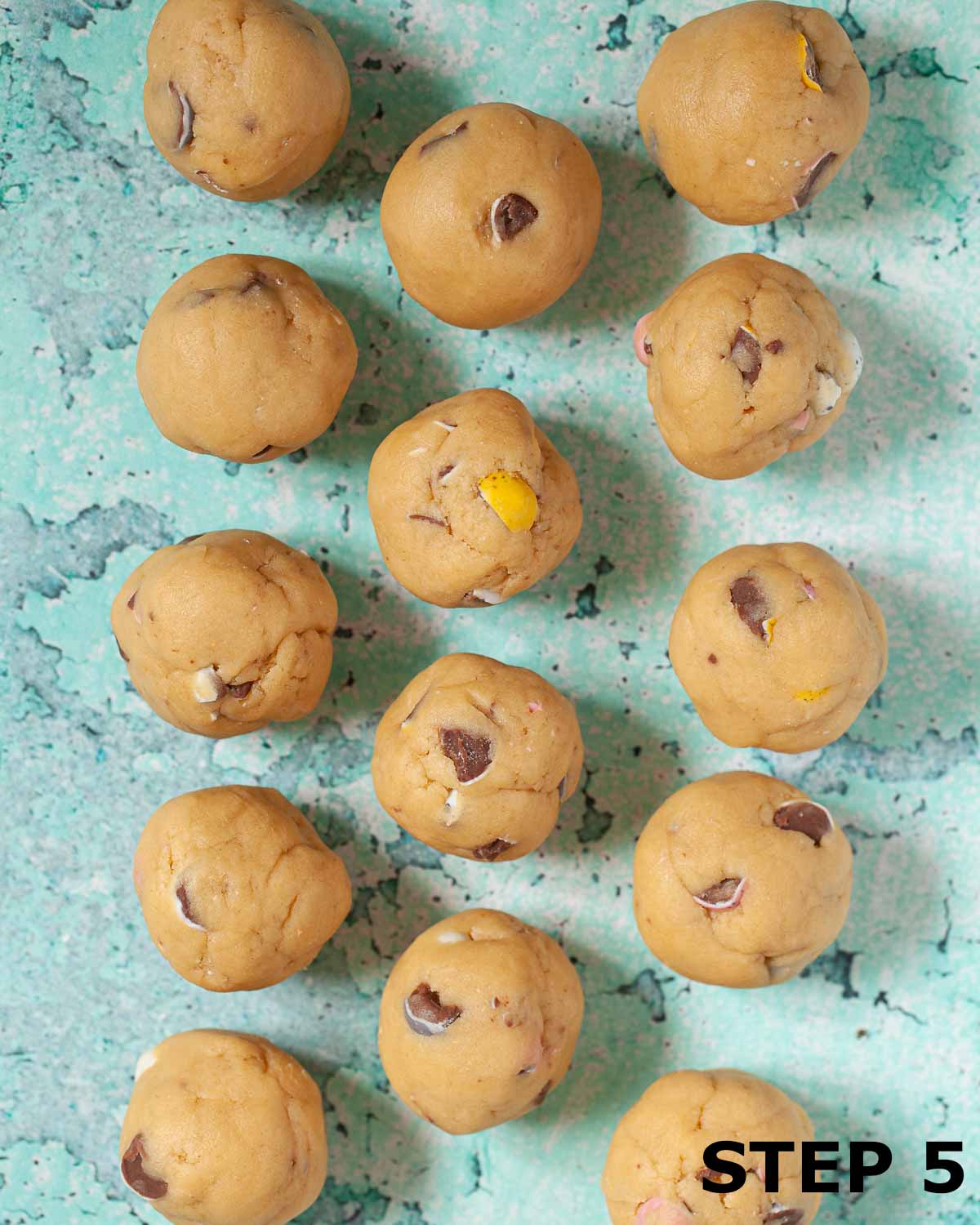 Balls of cookie dough containing crushed Mini Eggs on a baking sheet.