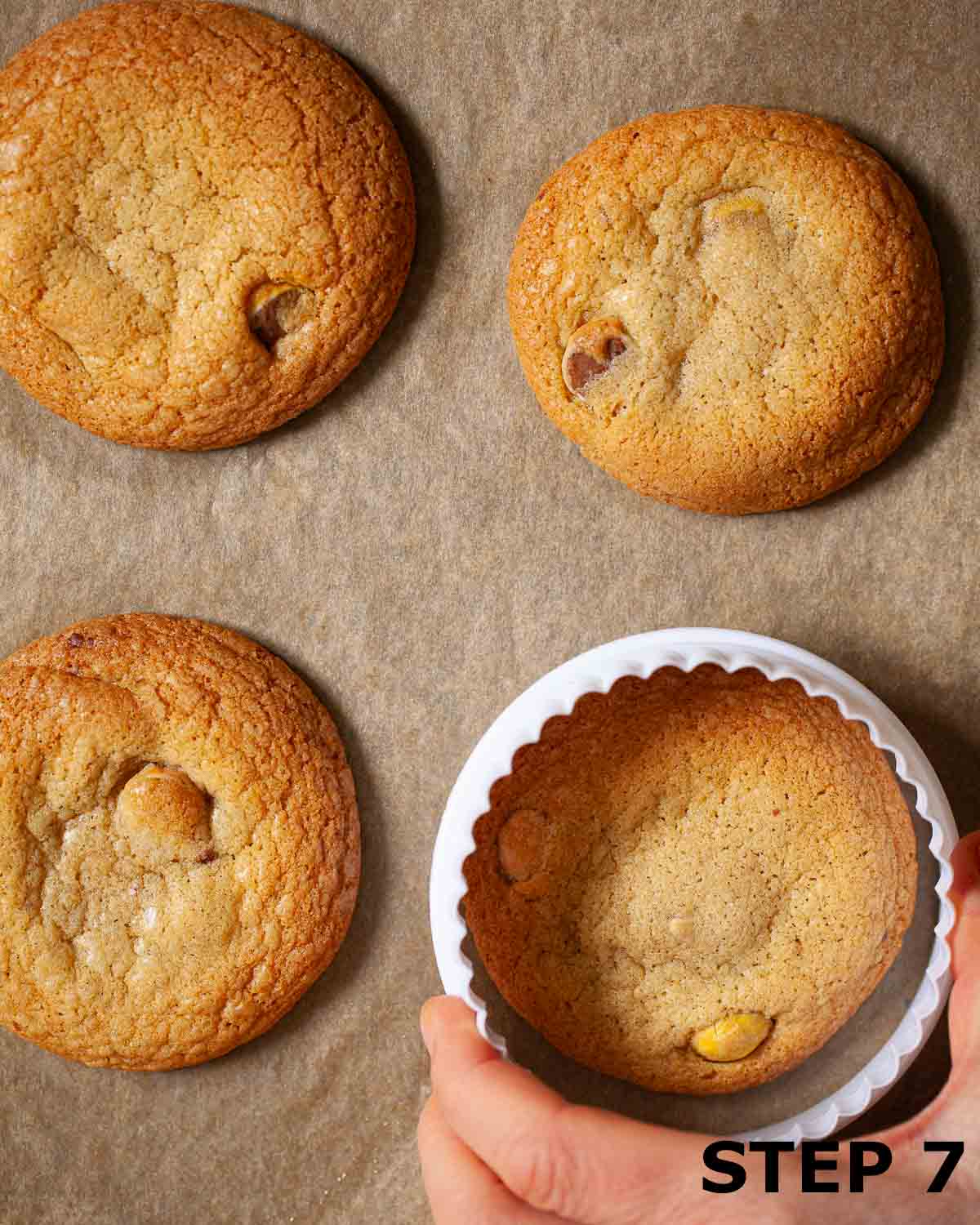 A person shaping freshly baked cookies into circles using a cookie cutter.