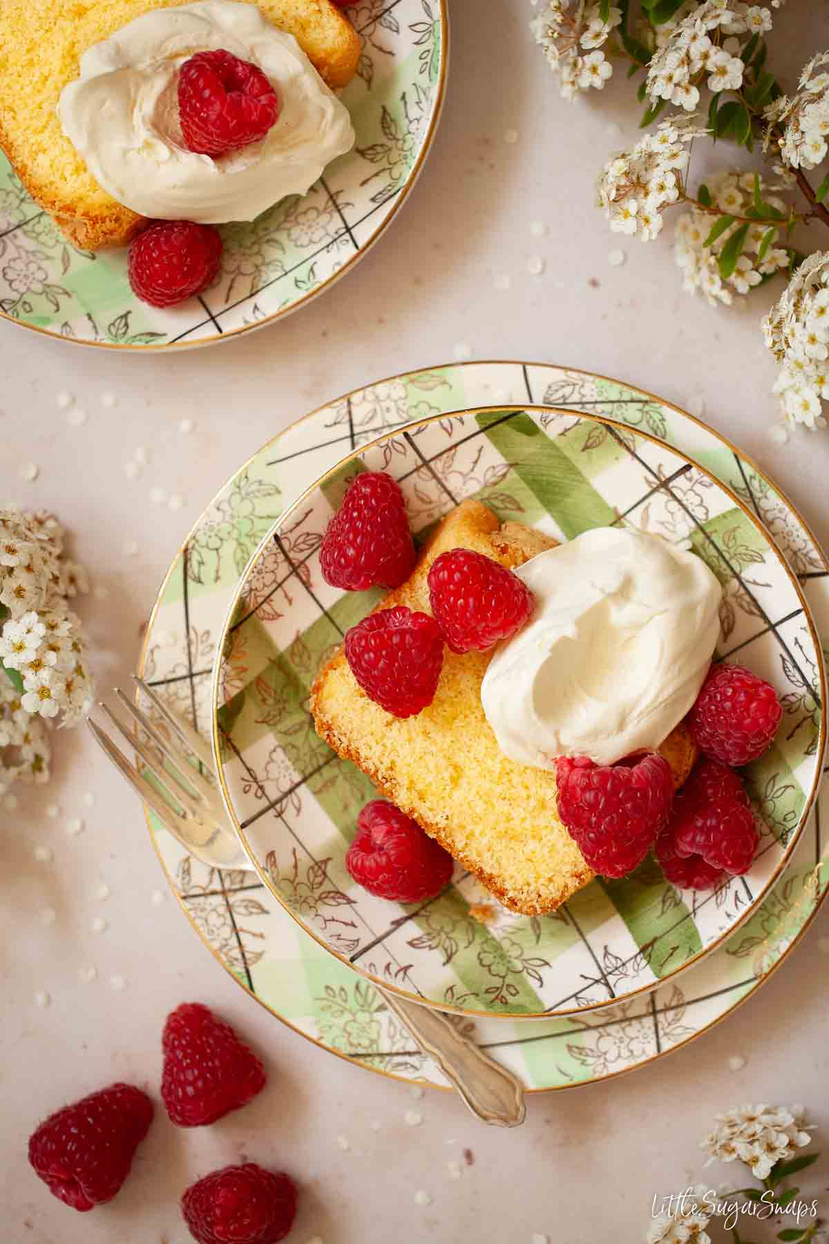 Cornflour cake served with whipped cream and raspberries on green plates.