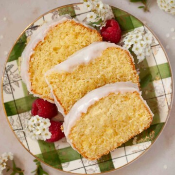 Three slices of iced Leicester sand cake on a plate with flowers and raspberries.