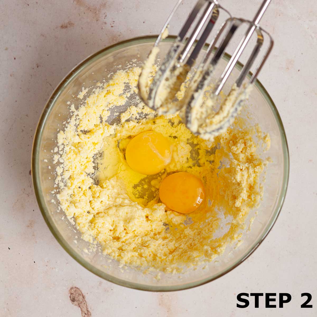 Two eggs in a mixing bowl with creamed butter and sugar.