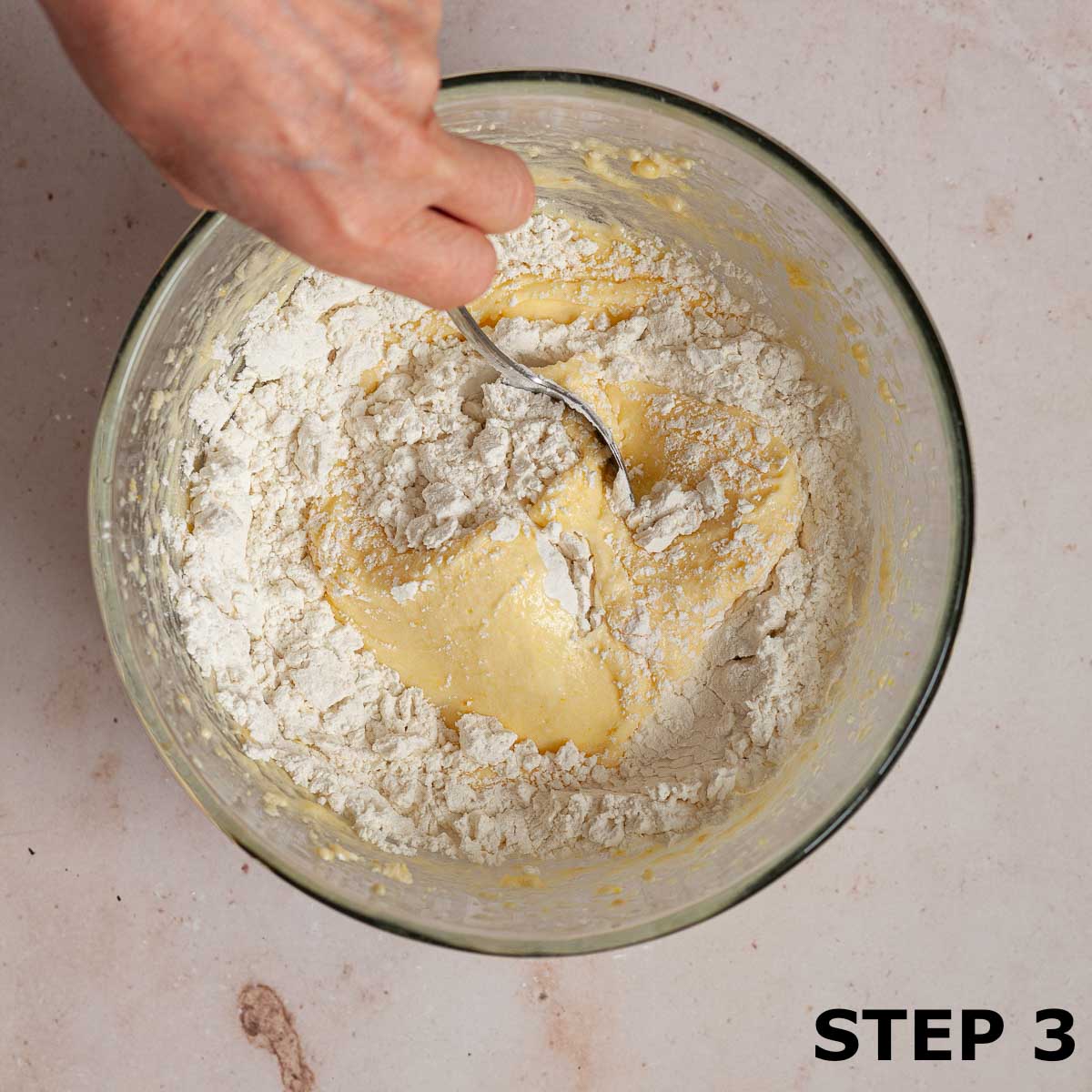A person folding flour and cornflour into batter for sand cake.