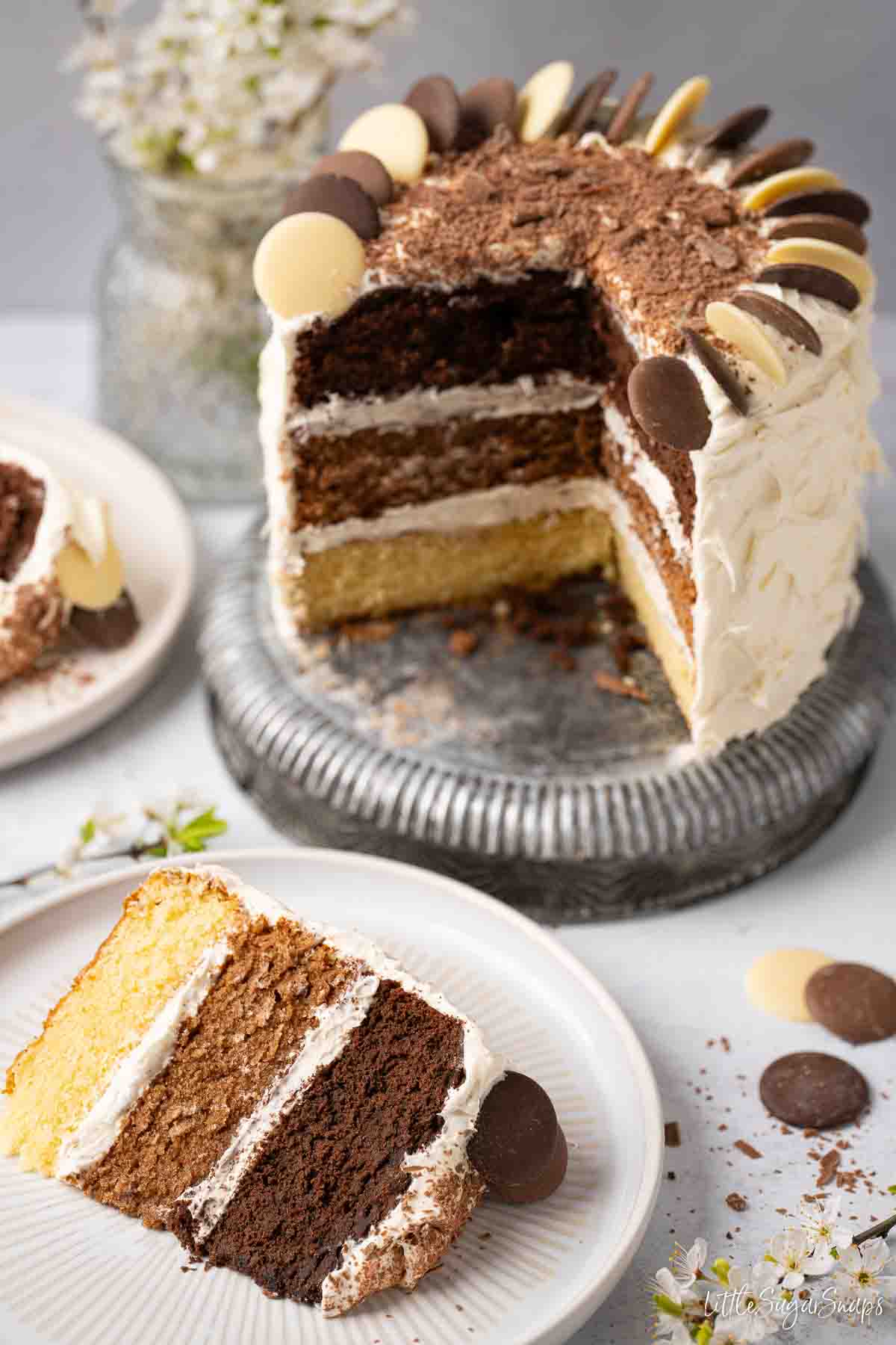 Triple chocolate layer cake with slices cut and on plates. Featuring white, milk and dark chocolate layers.