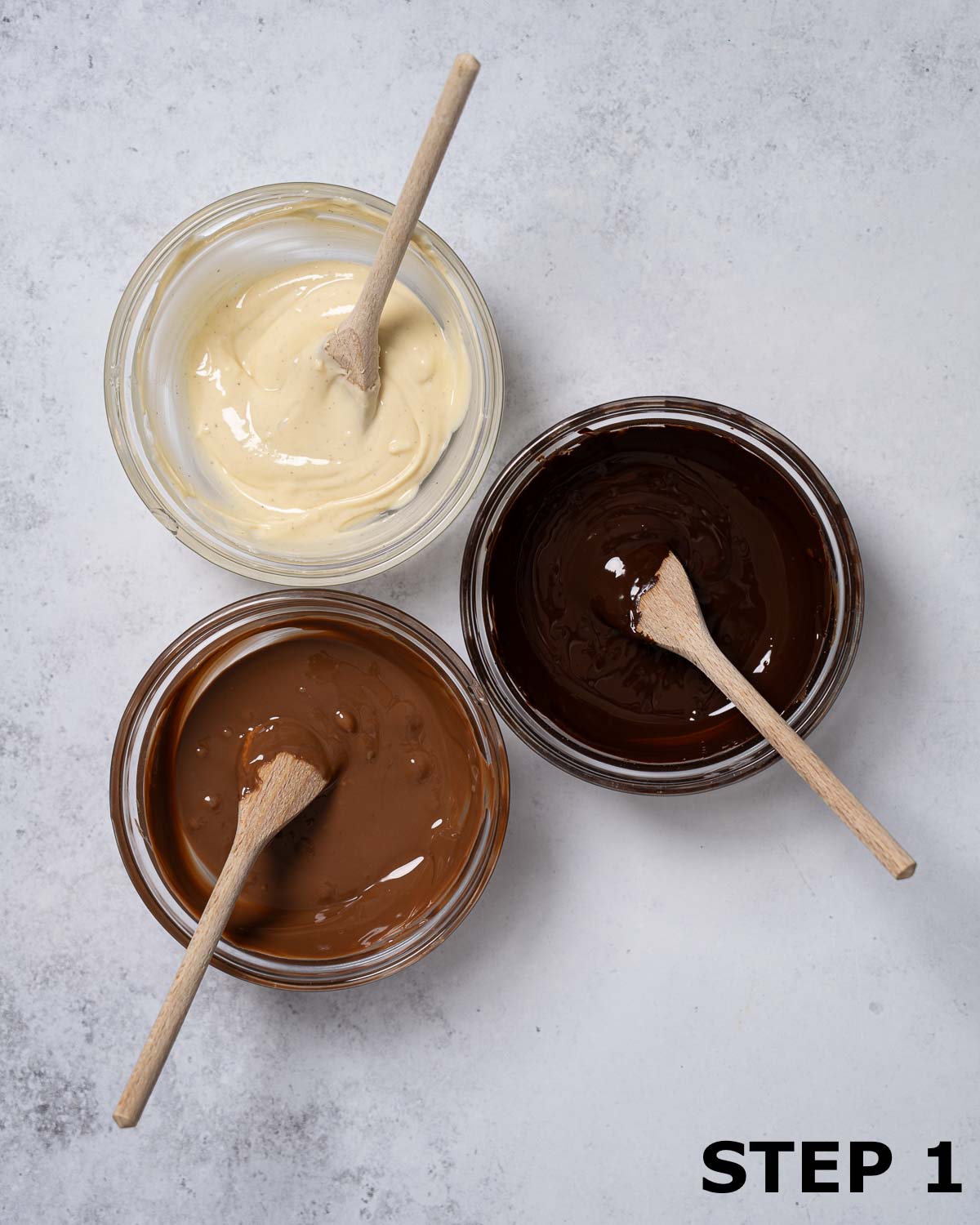 Three bowls of melted chocolate (white, mik and dark) with small wooden spoons in them.