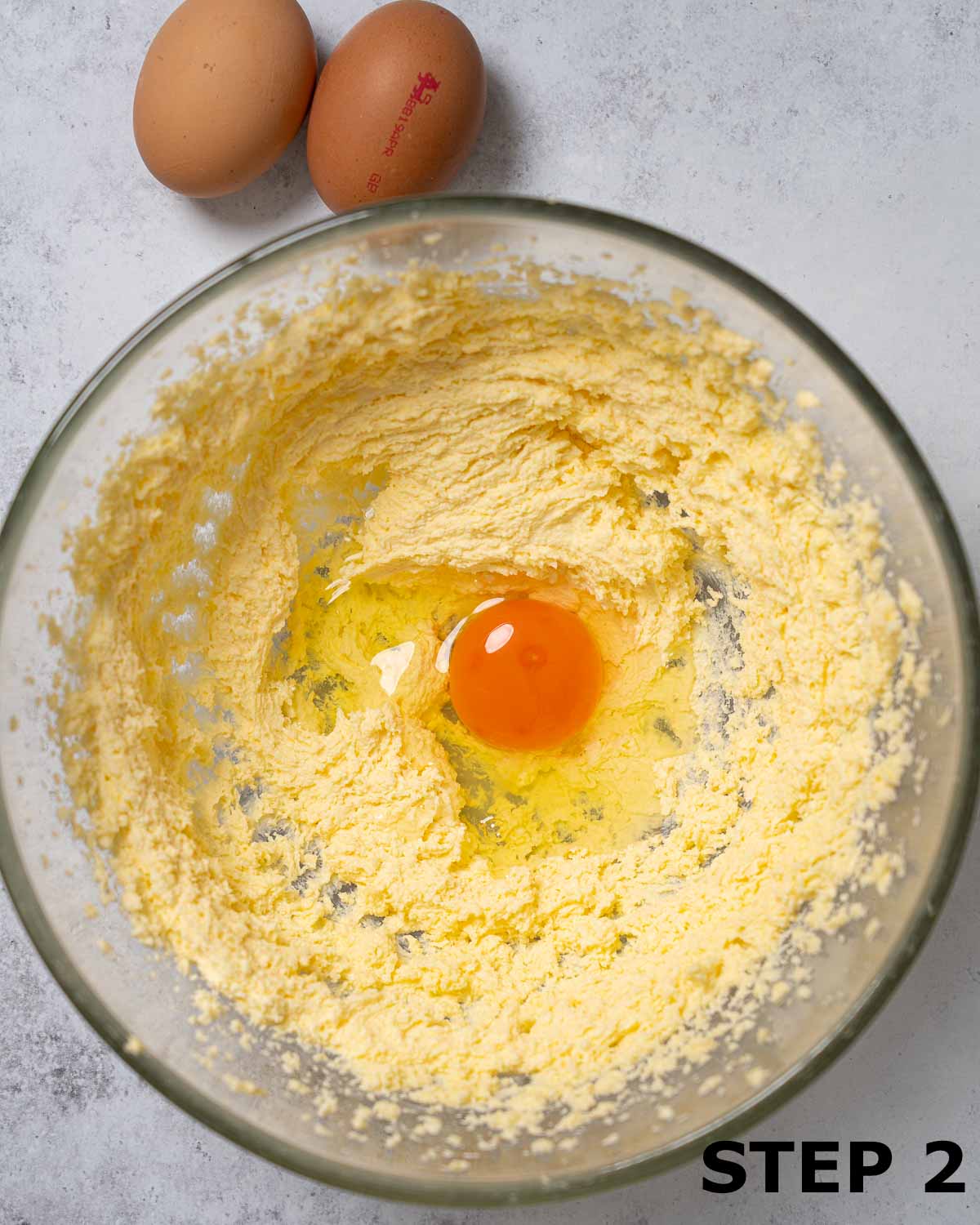 An egg about to be mixed into creamed butter and sugar.