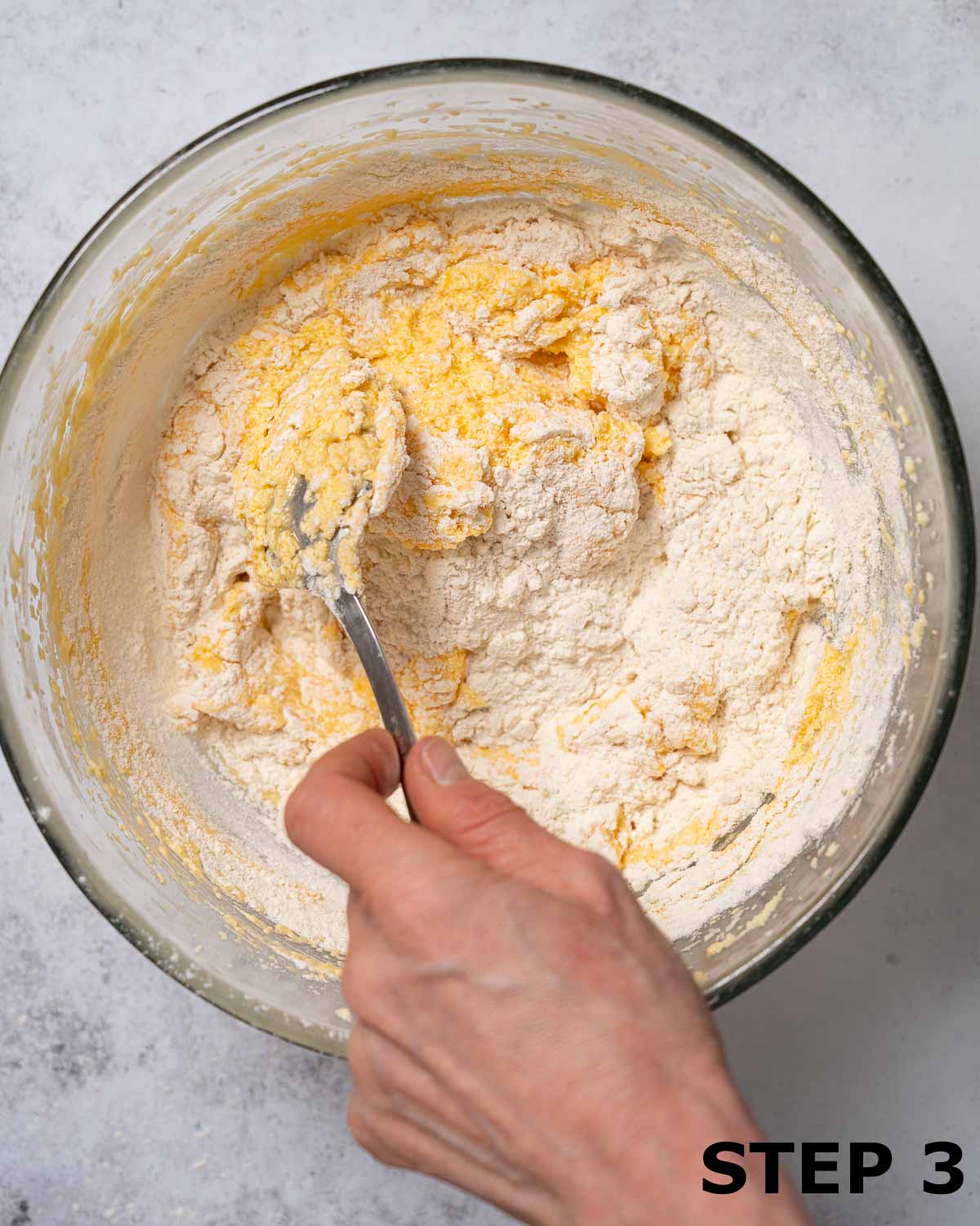 A person mixing flour into cake batter with a metal spoon.