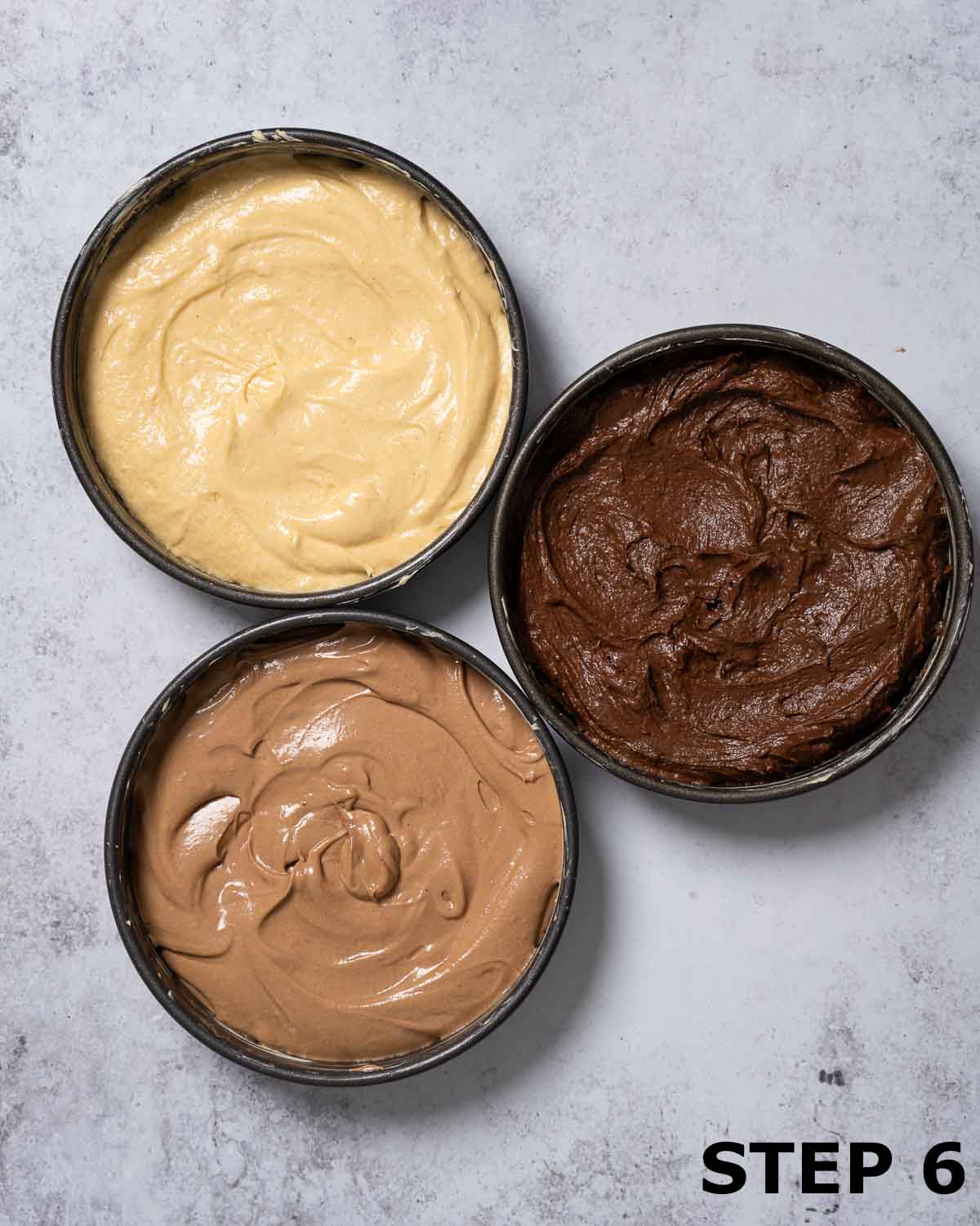 Cake batter flavoured with white chocolate, milk chocolate and dark chocolate in three baking tins.
