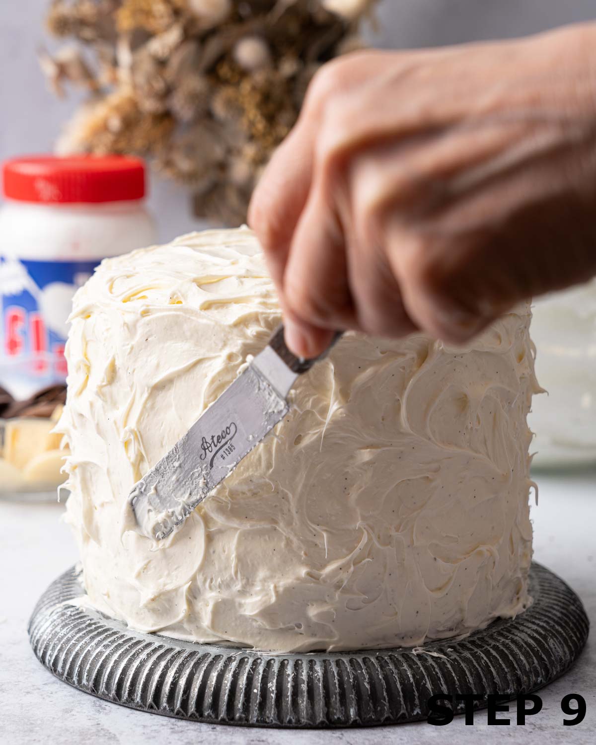 A person adding a pattern to the buttercream on a three layer cake.