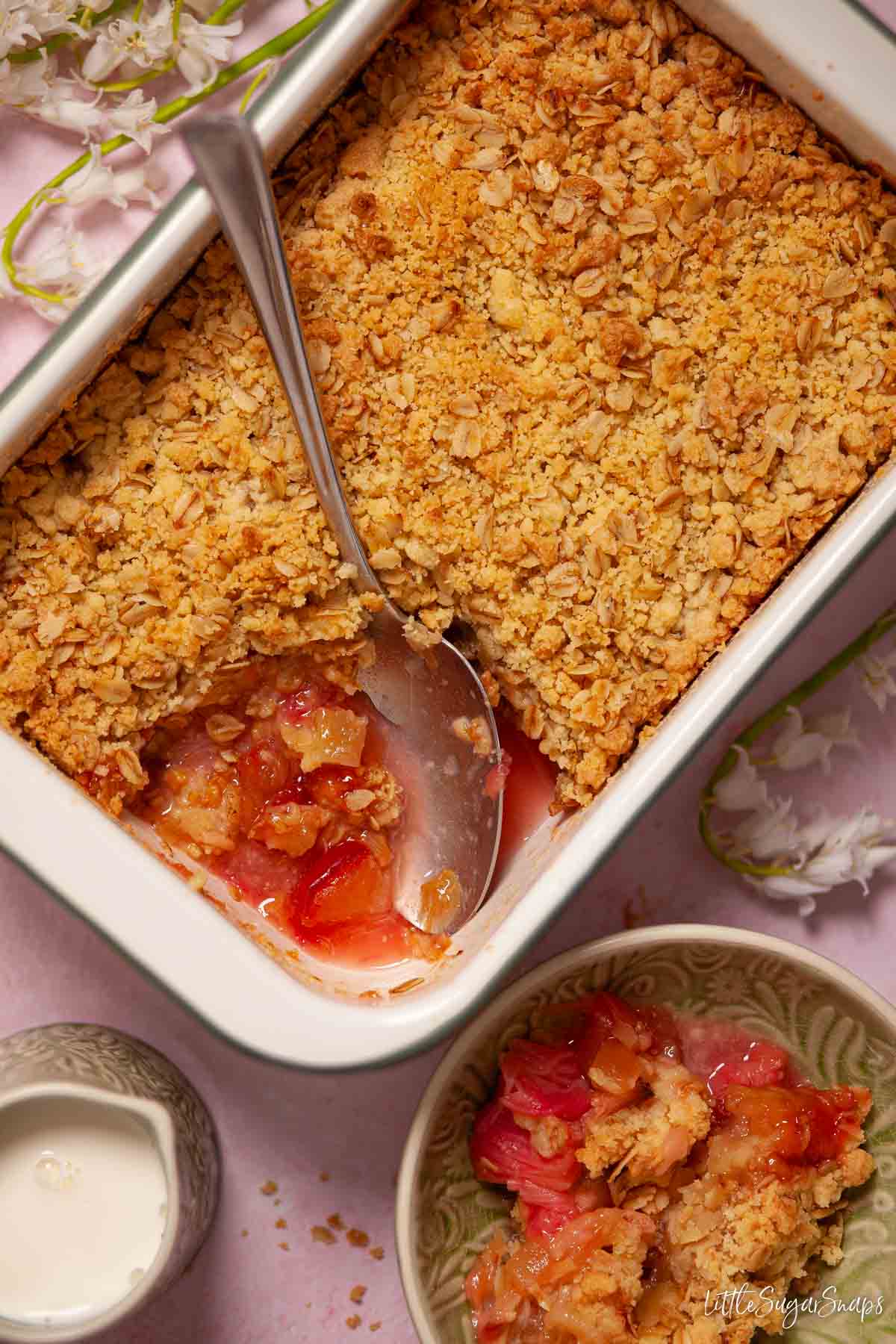 Apple rhubarb crumble being served from a large baking dish into bowls.