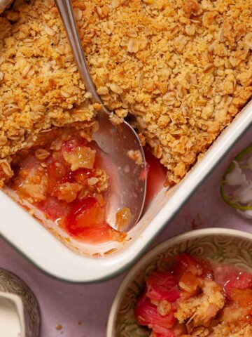 Apple & rhubarb crumble with ginger being served from a large baking dish into bowls.