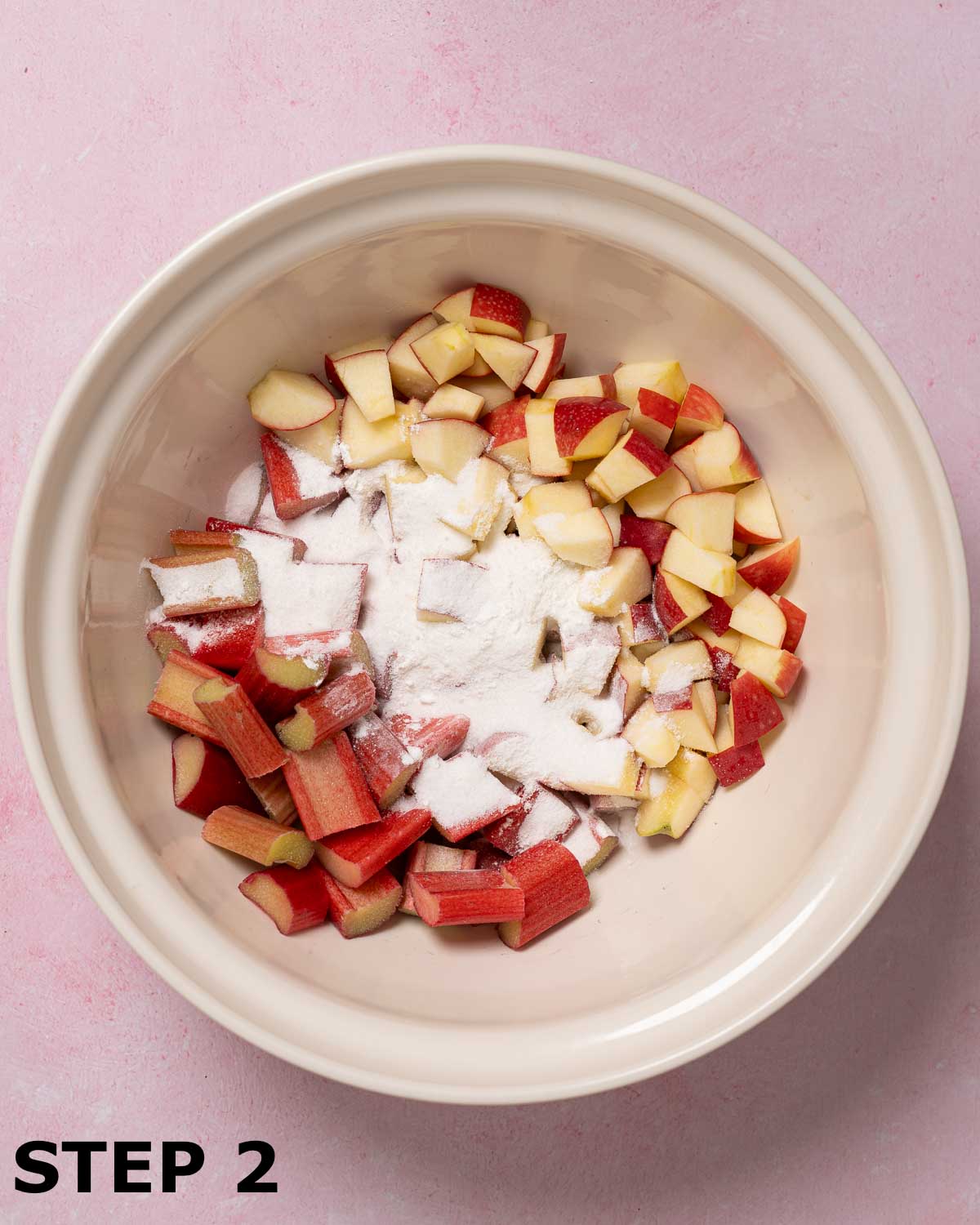 Chopped appkle and rhubarb in a mixing bowl with cornflour and sugar sprinkled on top.