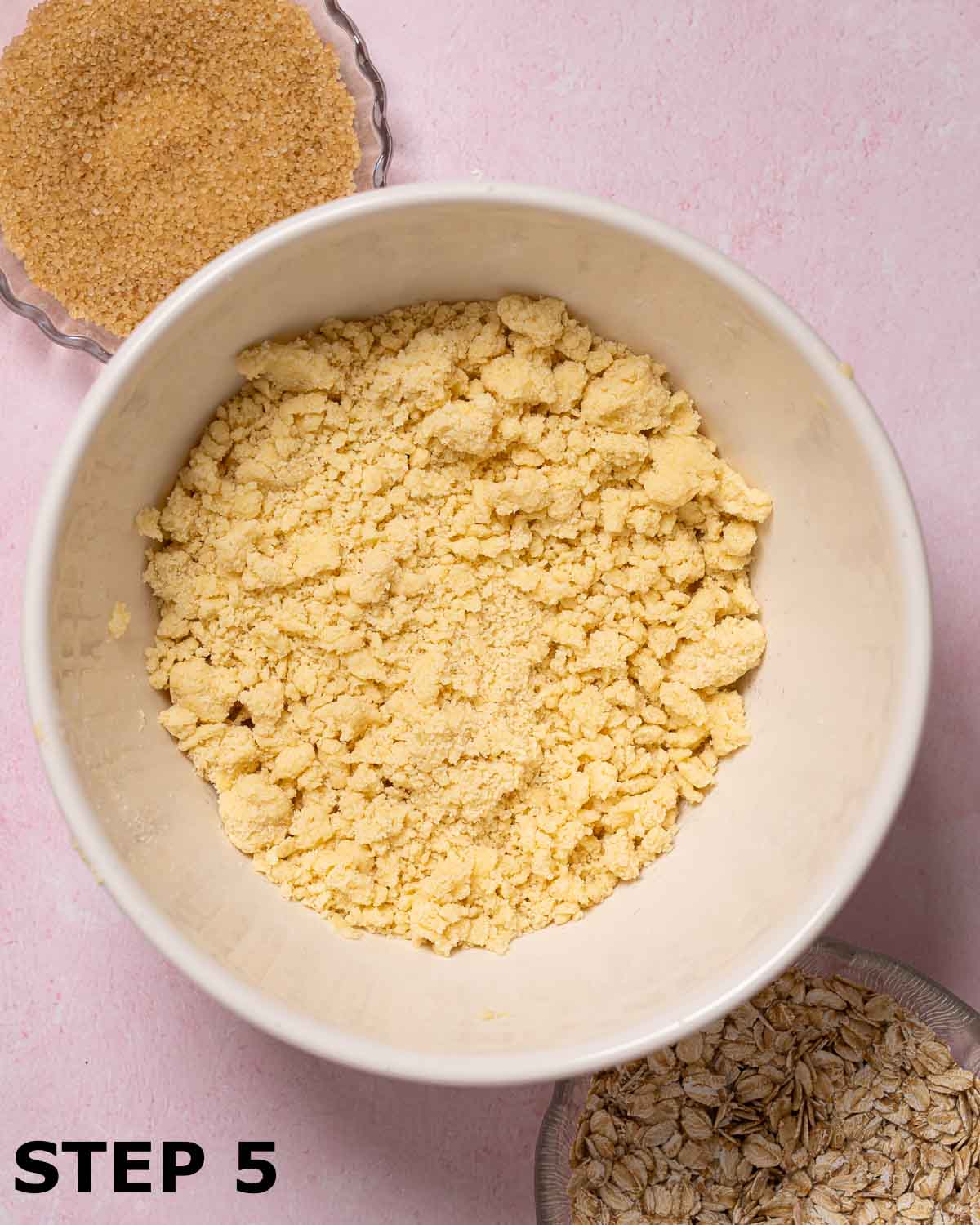 Crumble topping mixture in a mixing bowl with Demerara sugar and oats alongside.