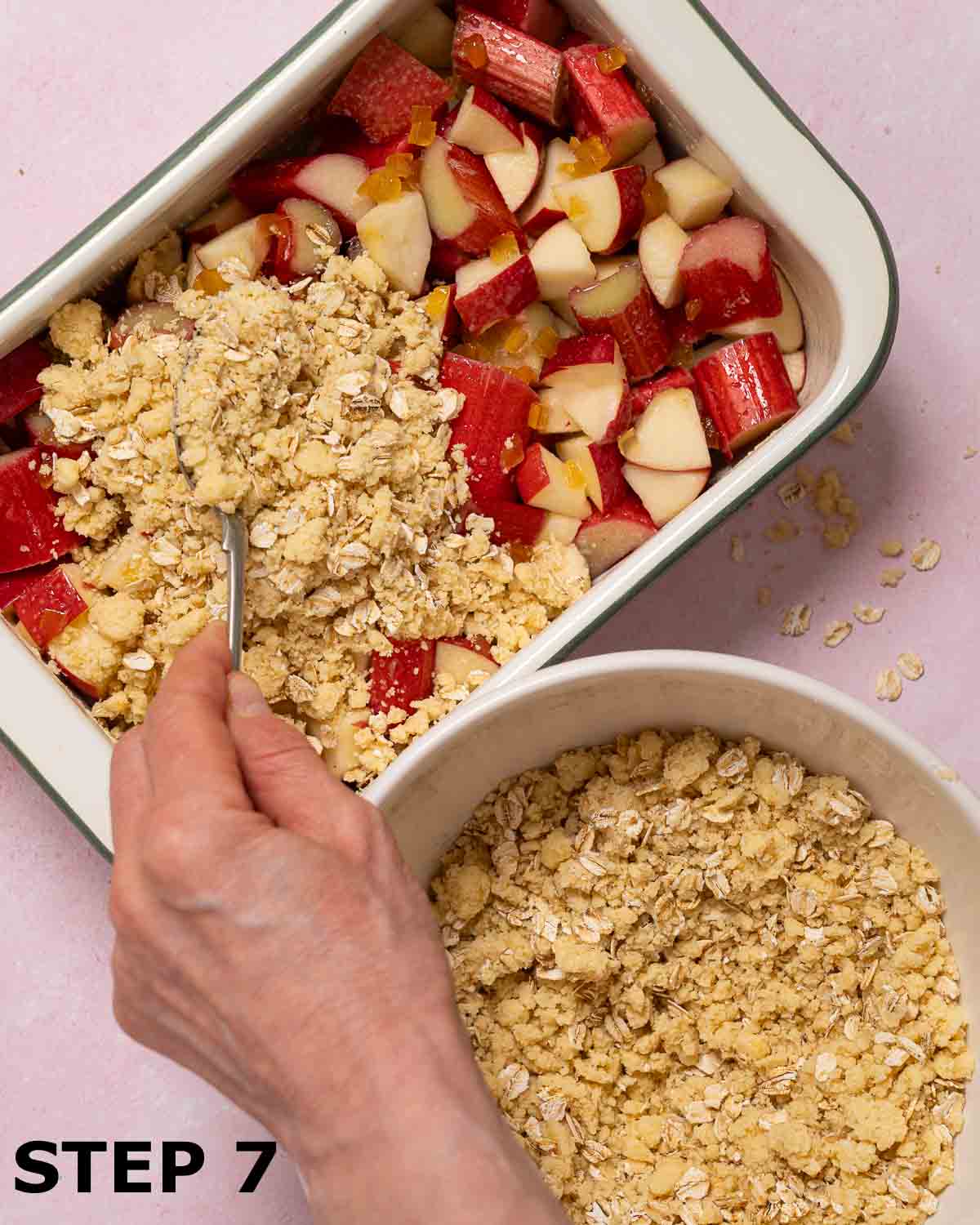 A person spooning crumble topping over rhubarb and apple crumble filling.