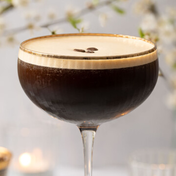 A caffe shakerato in a cocktail glass with a gold rim and garnished with coffee beans.