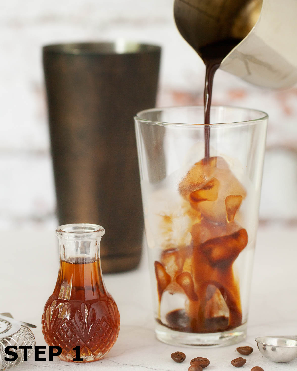 Espresso being poured over ice in a cocktail shaker glass.