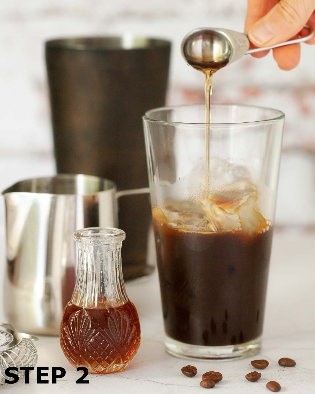 Syrup being added to a cocktail shaker containing ice and espresso coffee.
