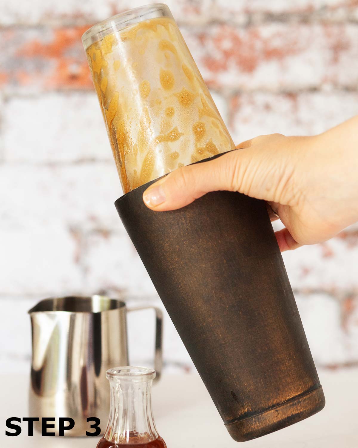 A person shaking a caffe shakerato in a cocktail shaker.