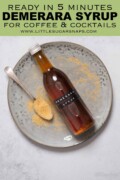 A bottle of Demerara syrup on a plate with a spoon and sugar alongside with text overlay.