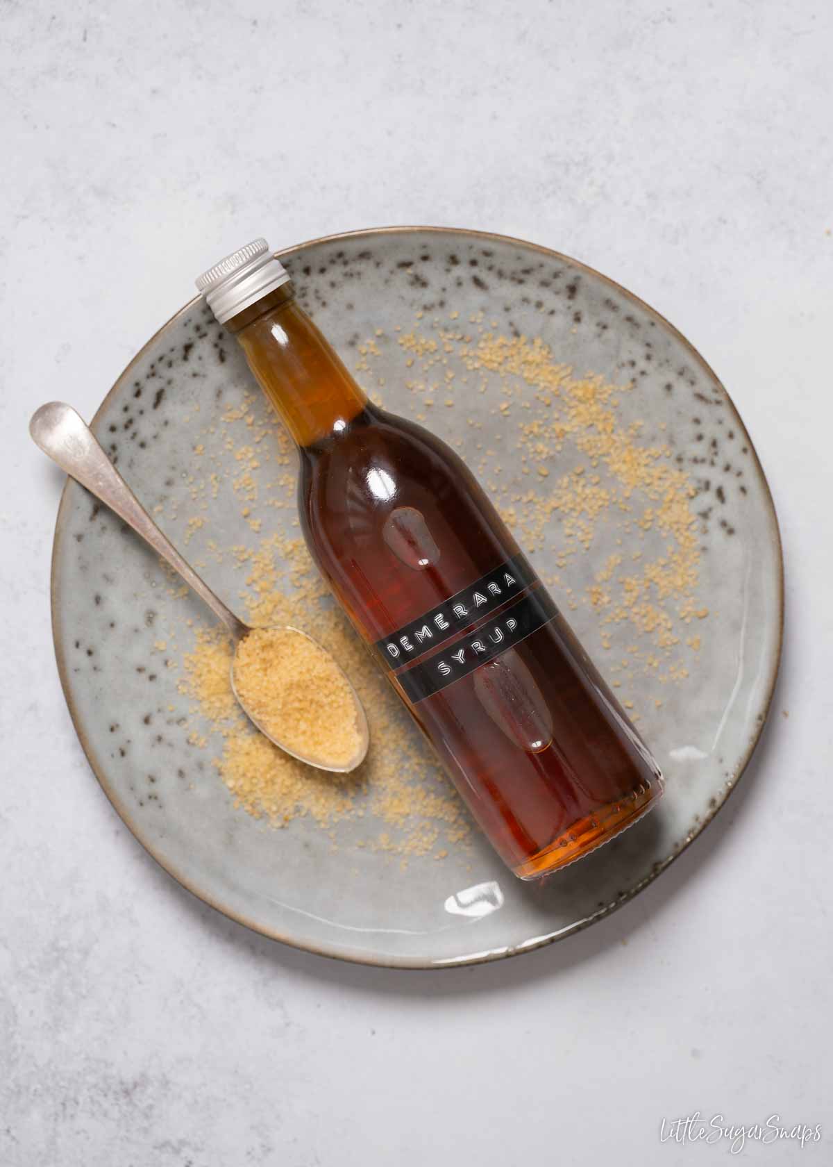 A labelled bottle of Demerara syrup on a plate with a spoon and sugar alongside.