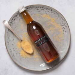 A labelled bottle of Demerara syrup on a plate with a spoon and sugar alongside.