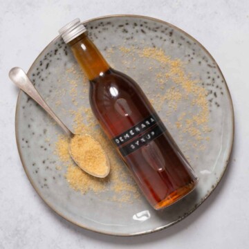 A labelled bottle of Demerara syrup on a plate with a spoon and sugar alongside.