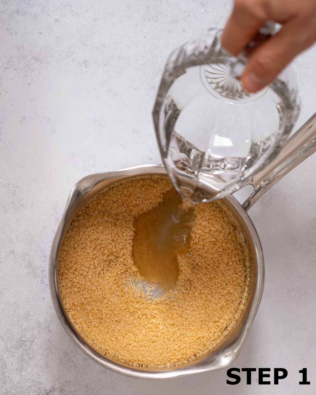 A person pouring water into a pan with Demerara sugar in it.