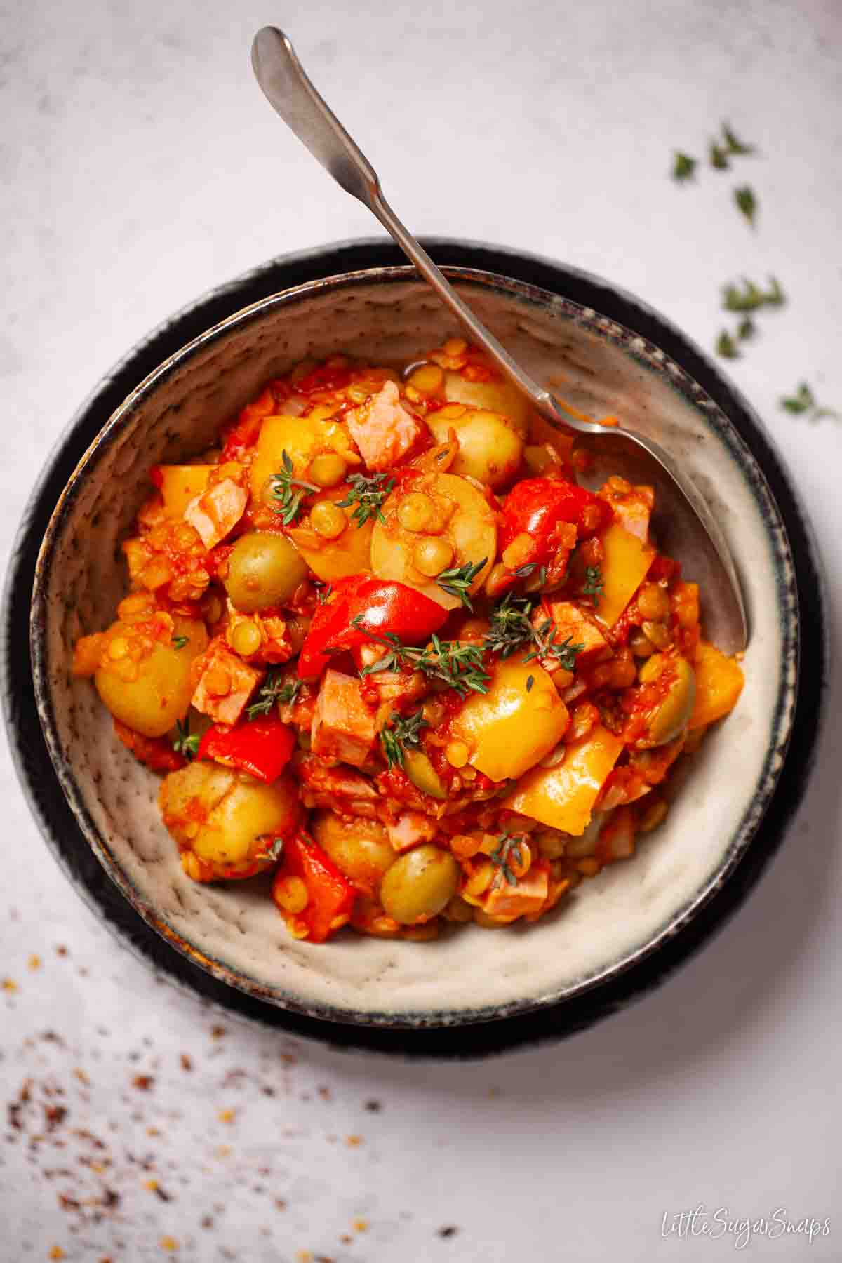 A bowl of lentil and ham stew with potatoes on a grey background with a spoon in the bowl.