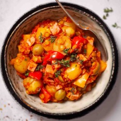 A bowl of lentil and potato stew with ham, olives and peppers.
